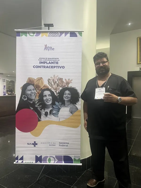 Dr. Sérgio ao lado do banner da oficina de qualificação em implante contraceptivo