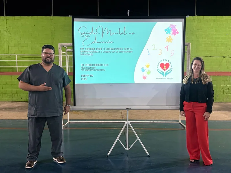 Dr. Sérgio e uma colega ao lado da tela Saúde Mental na Educação, em um ginásio