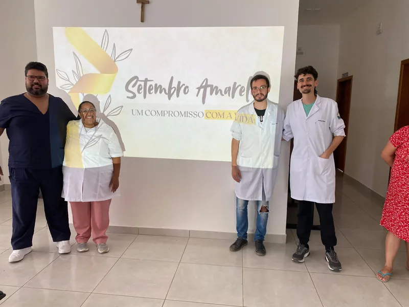 Dr. Sérgio com colegas de jaleco diante da tela Setembro Amarelo